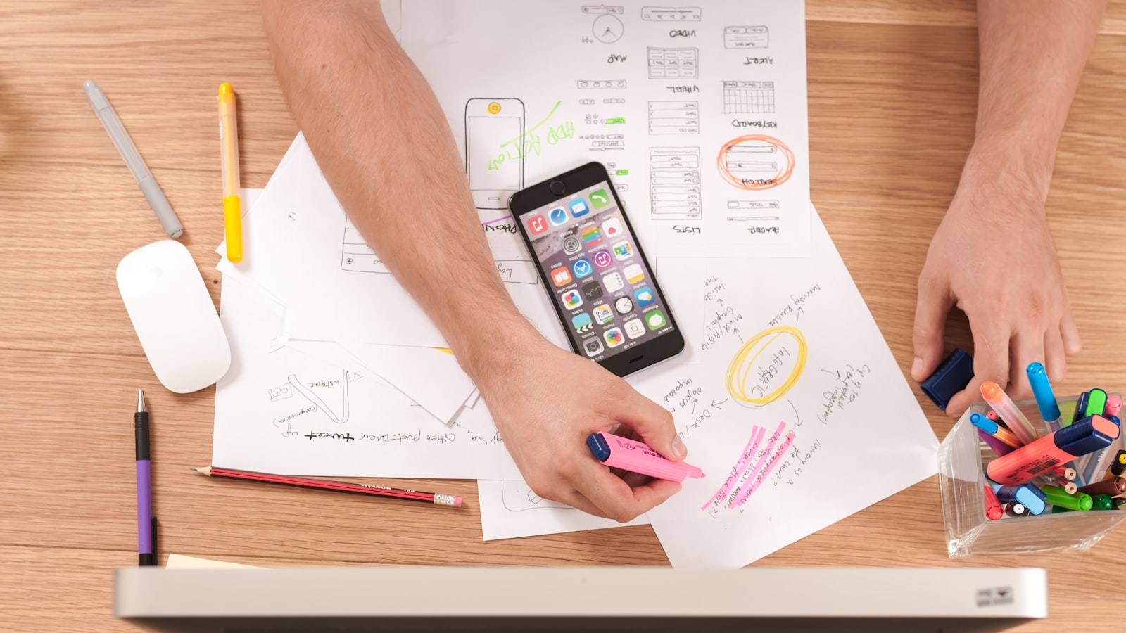A hand holding a smartphone showing an app, with papers on a desk