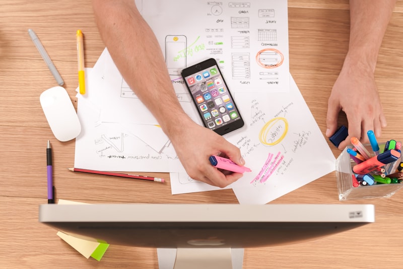 A hand holding a smartphone showing an app, with papers on a desk
